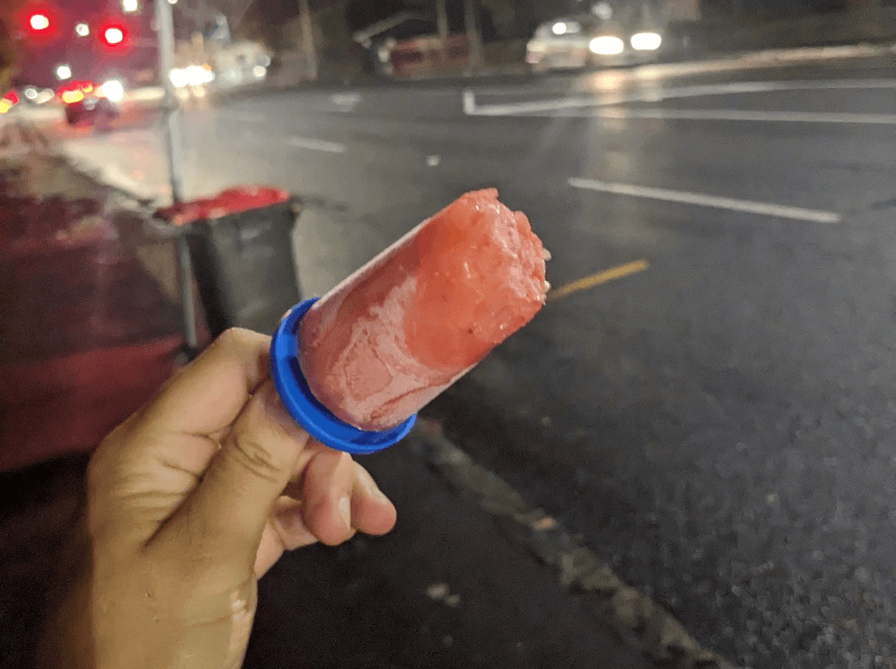 a hand holding an iceblock with a wet road in the background