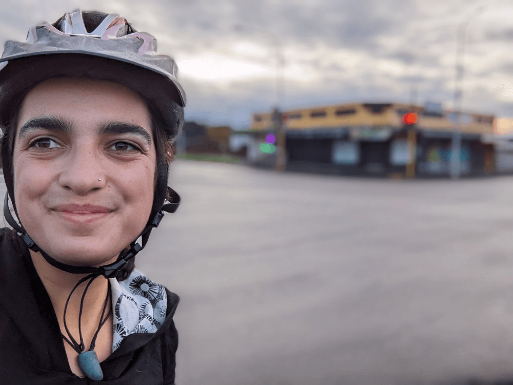a smiling woman wearing a bike helmet with tarmac behind her