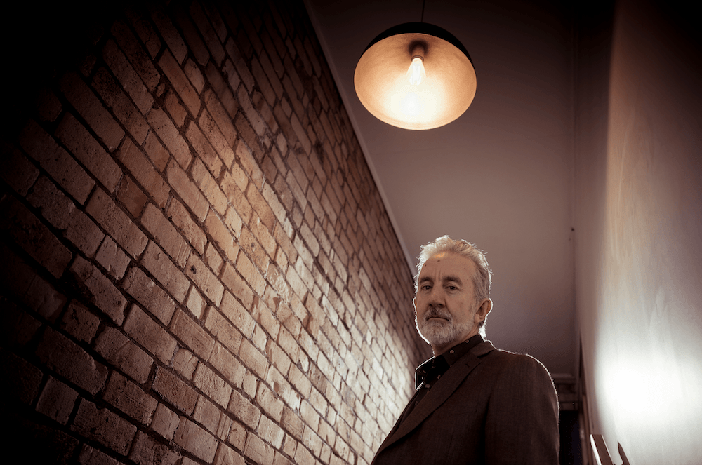 Nigel Latta next to a brick wall with gloomy lighting.