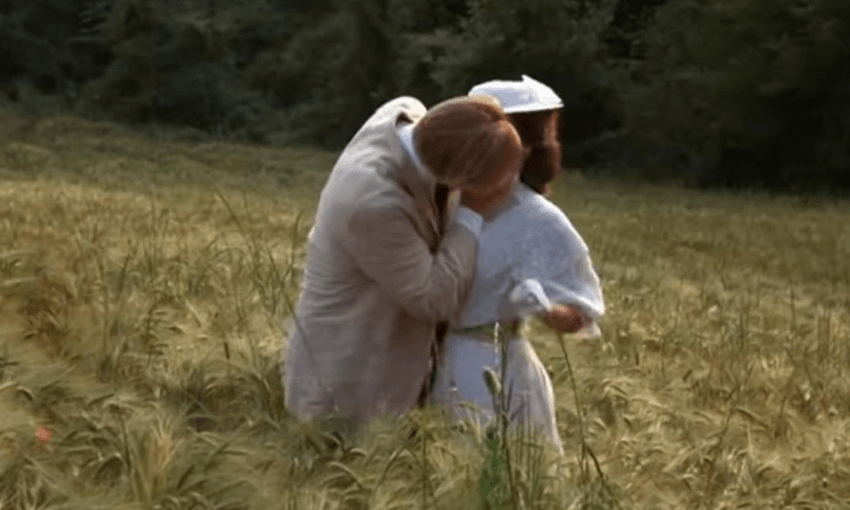 A man and a woman in period costume, kissing in a poppyfield.