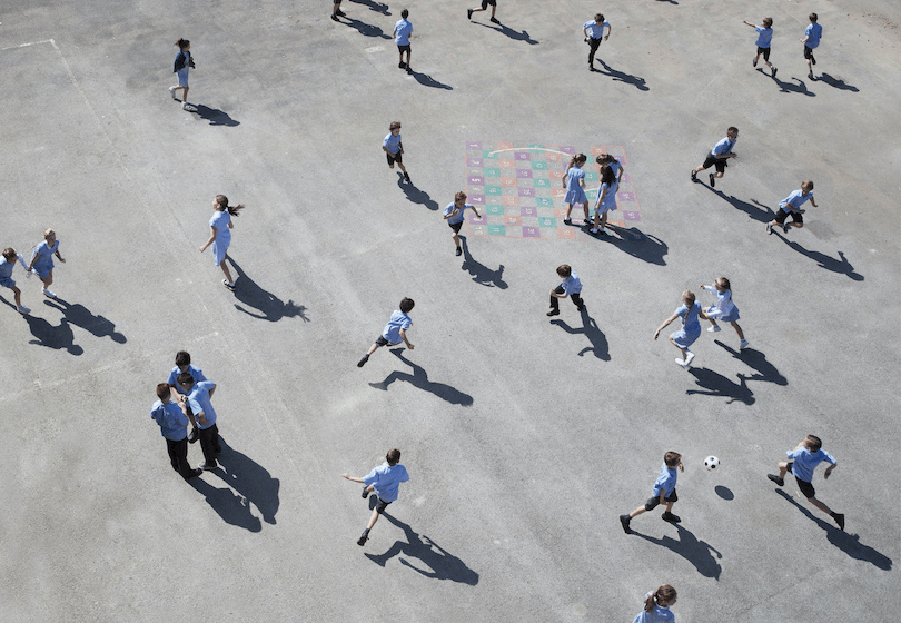 an overhead view of children running around on the concrete of a school playground
