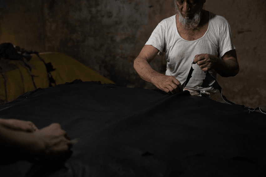 a dark background with hands workingon fabric, perhaps leather. 