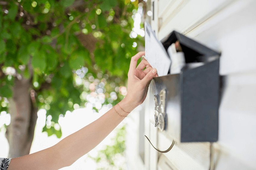 a light skinned hnd reaches into a mailbox with a tree in the background