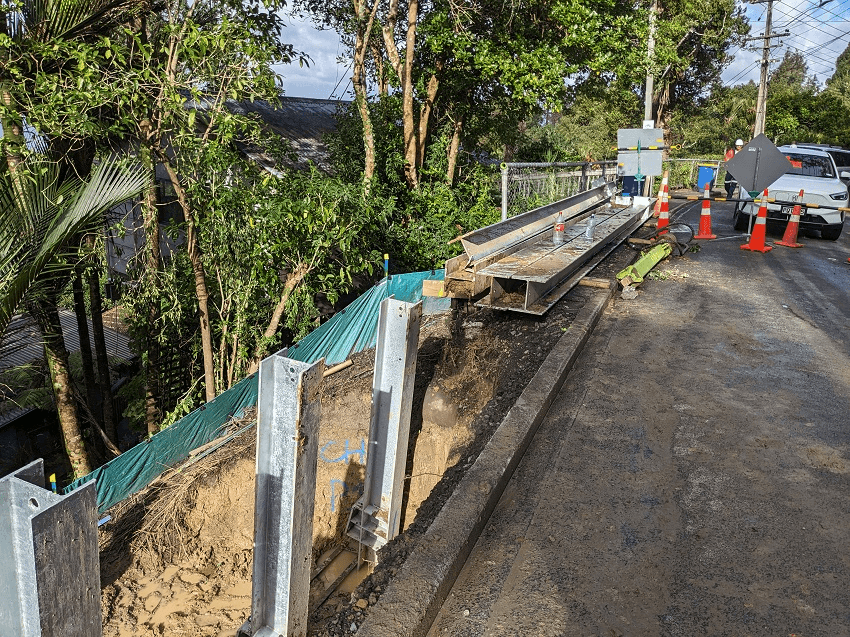 a corner of road with two big ol' poles plunged into the empty space to build a future retaining wall