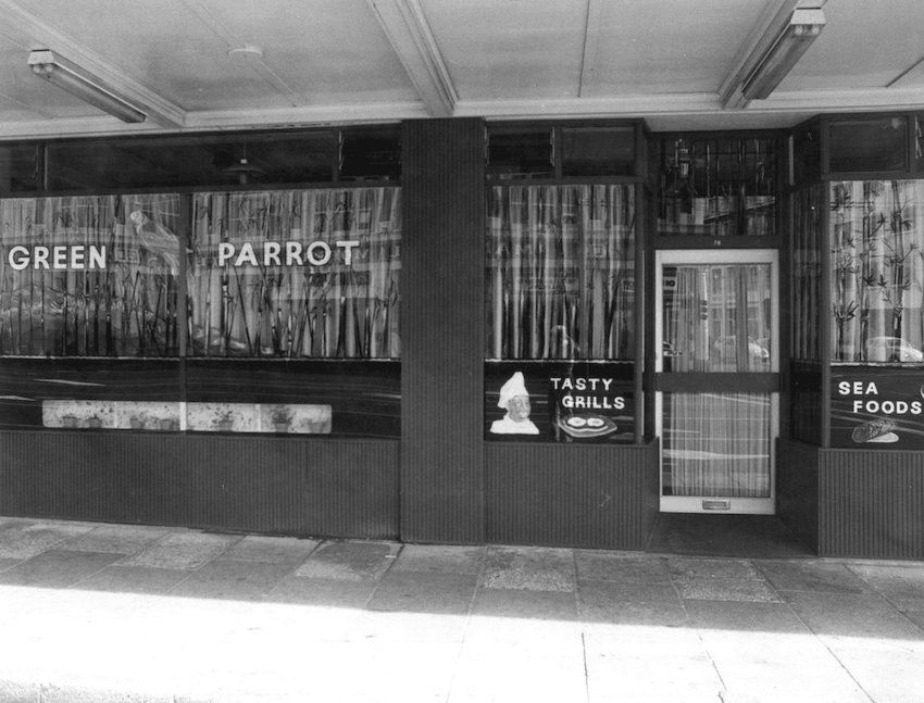 A black and white image of the front of the Green Parrot Cafe in Wellington. "Tasty Grills" and "Seafoods" is written on the windows.