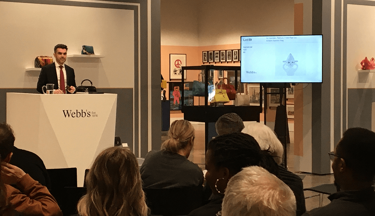 Auctioneer by digital screen showing lot 59 - the large diamond ring