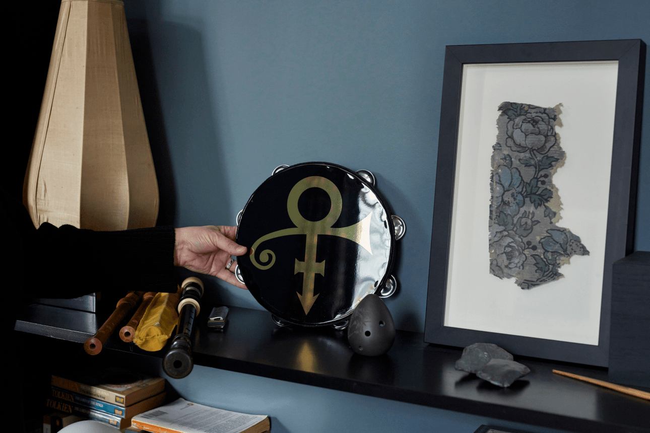 Victoria Kelly's hand holding a black lacquered tambourine bearing the symbol of late R&B musician, Prince.