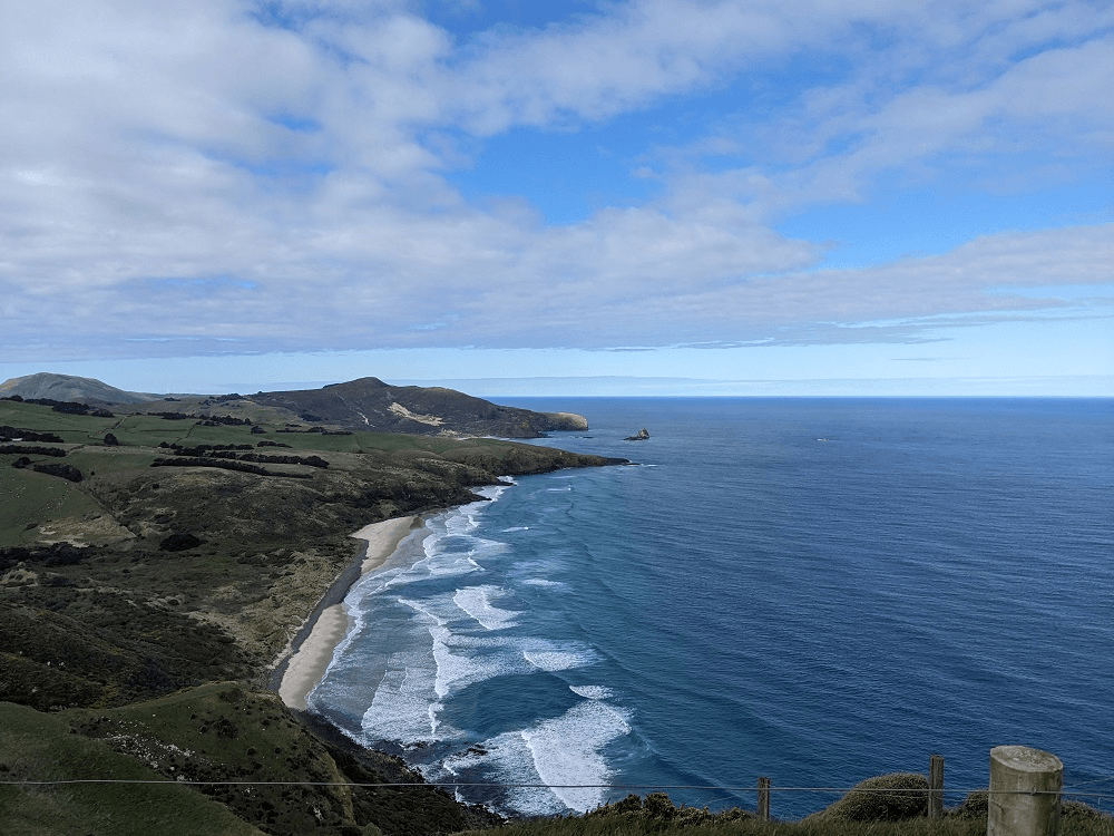a blue sea and land with frothy breakers visible and hills too
