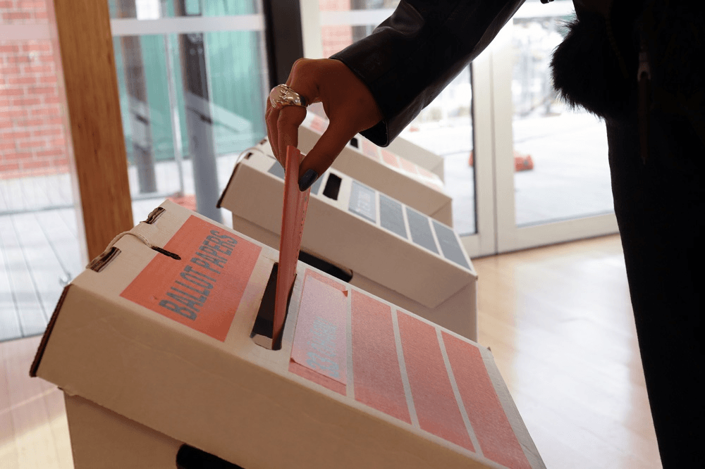 a hand placing a ballot in a box 