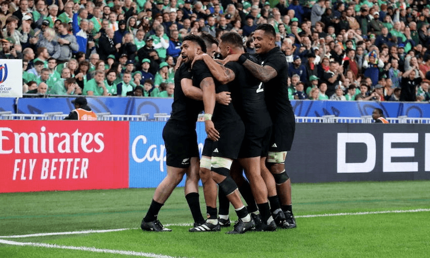 men wearing black tshirt and shorts jump in a field with lots of fans watching on