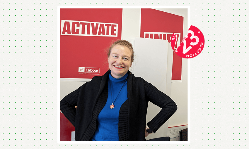 Rachel Brooking, a smiling white woman with a blue top, stands in front of Labour signs in the party's campaign office