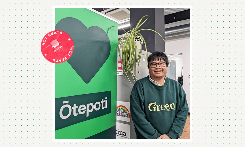 a filipino man in a green sweater staning next to a Green party sign with a plant dangling in his face 