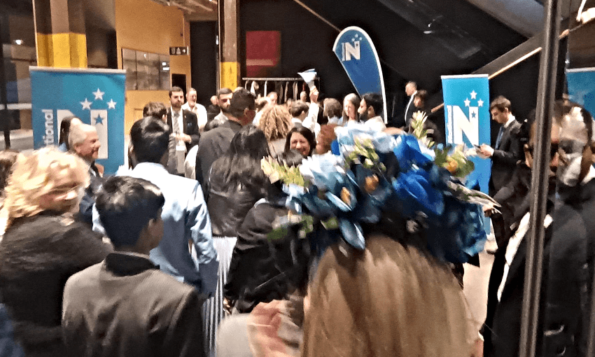 a big crowd of people in what looks like a hall with some national signs in the background