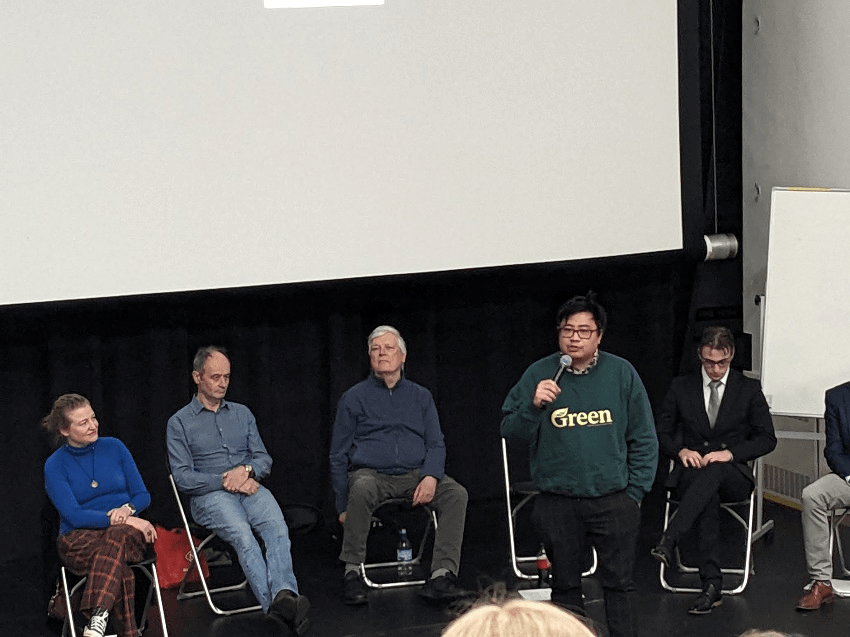 a man in a Green sweater in front of five other people, seated
