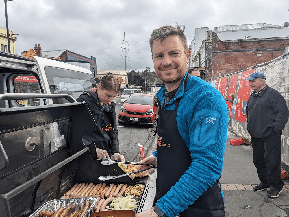 a man in a blue fleece shirt at a barbecue with a apron that says "south d-licious"