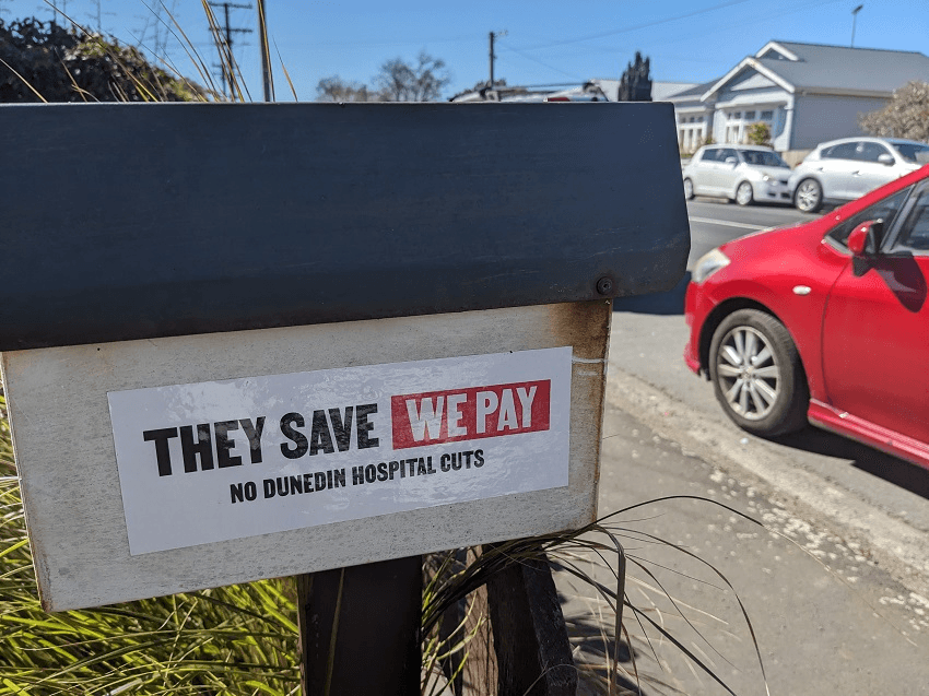 a letterbox with a sign saying "they save we pay no cuts to dunedin hospital"