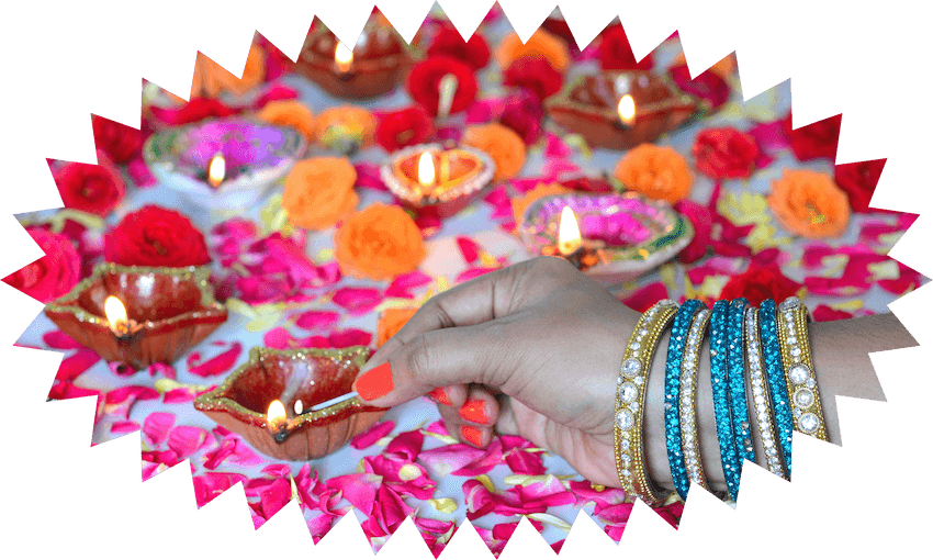 A woman's arm wearing many sparkly bangles, with painted orange nails, holds a match to light colourful diyas (small oil lamps) on a surface strewn with flower petals