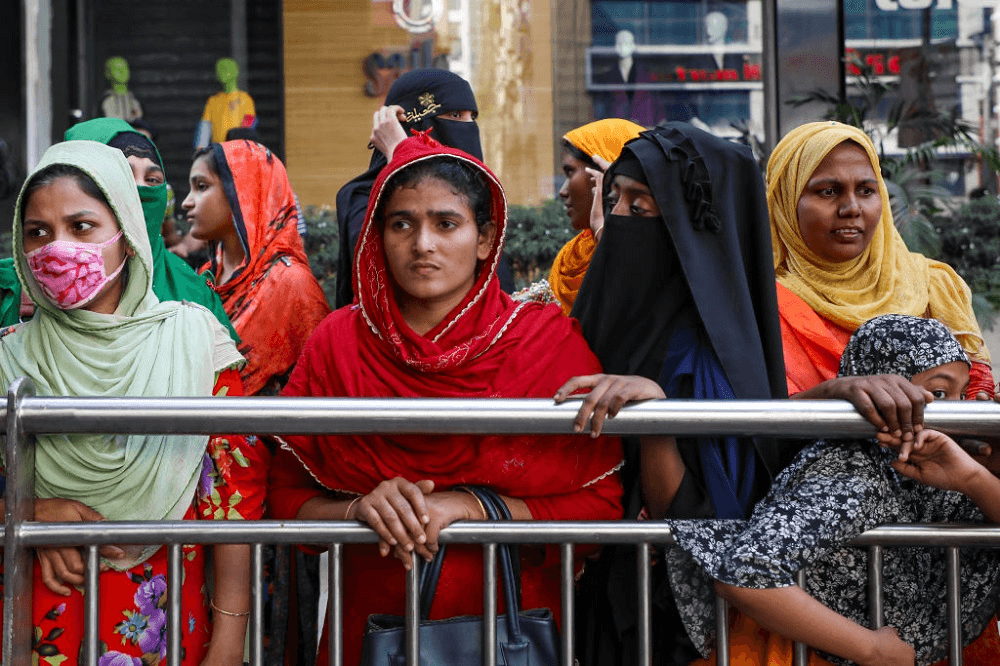 woman in colourful clothes and facemasks wearing head scarfs in front of a fence