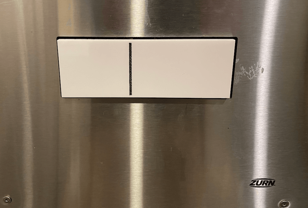 A toilet flush button clearly demarcated between full and partial flushes. 