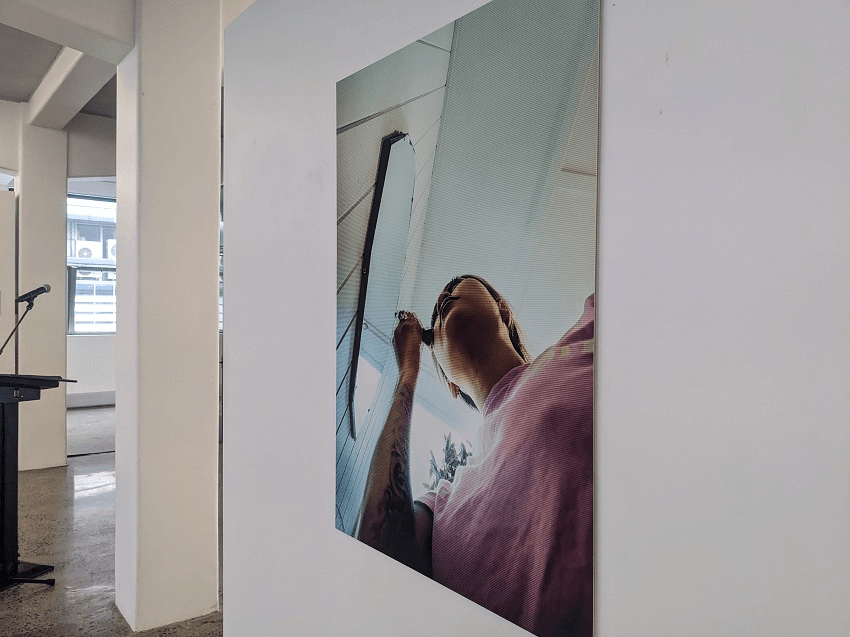 a white gallery wall and a woman applying mascary in a photo, looking blurry and pixelated
