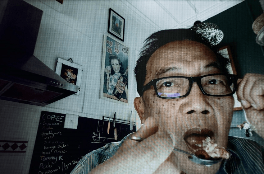 a middle aged Asian man in a pixealated surface with a spoon going to his mouth and revelections of a screen in his eyeclasses