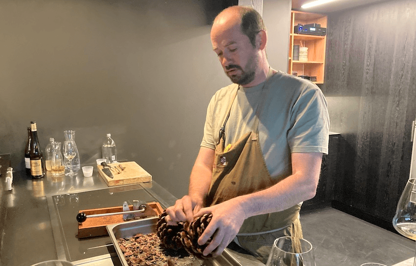 a man with an apron holdinga pine gone and a tray full of nuts