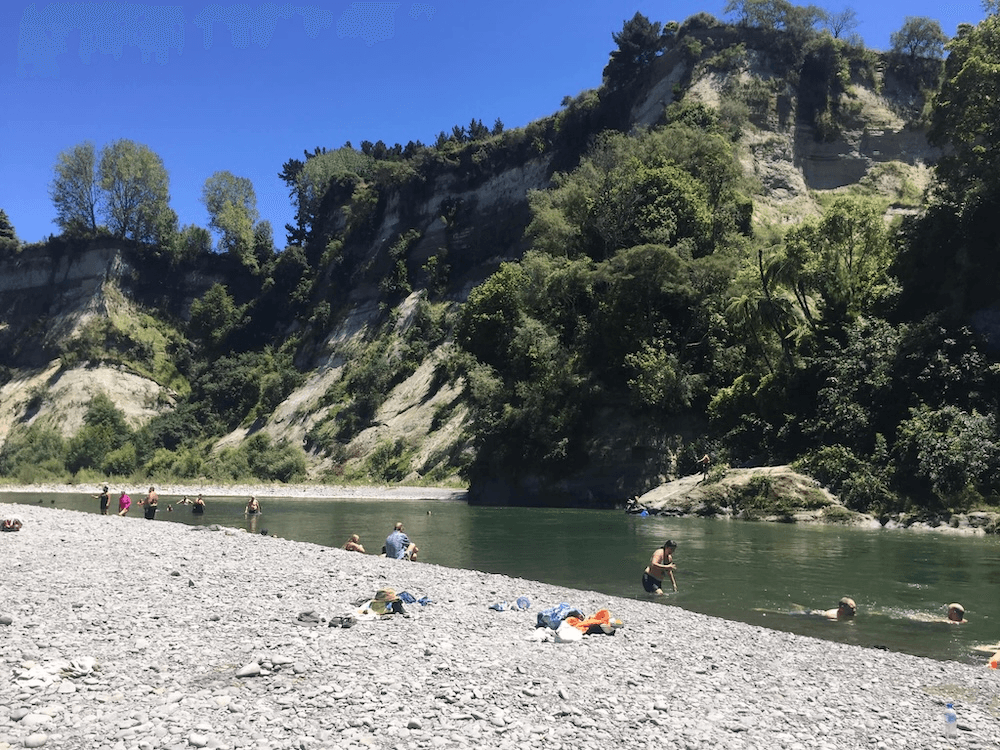 a green river with a rocky beach and lots of people swimming in the sunshine