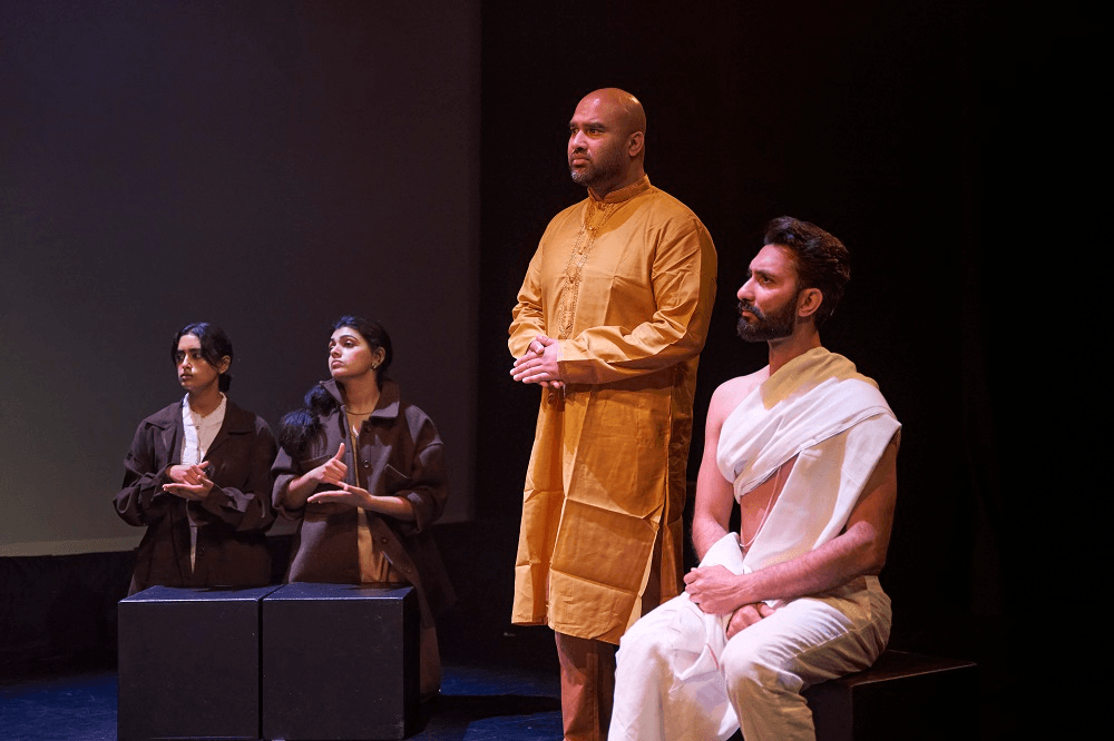 a black background and actors in an organge gold kurta and a white lungi slooking to the left