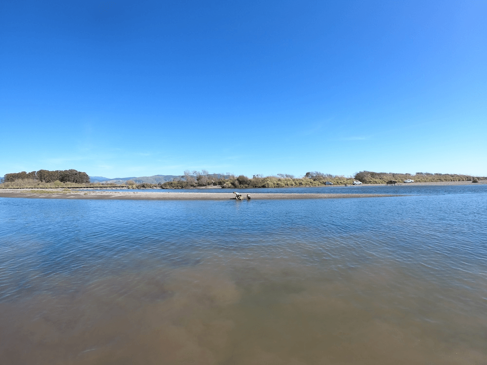 an astonishingly clear blue sky and sof blue water with three small kids on the otehr side of the shore playing in the sand