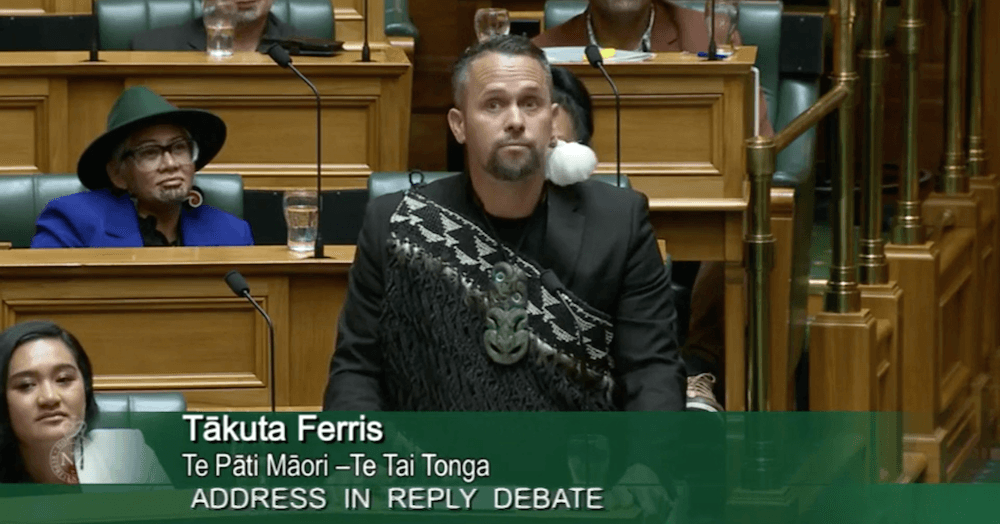 Tākuta Ferris giving his maiden speech in parliament wearing a hei tiki, cloak and feather earring.
