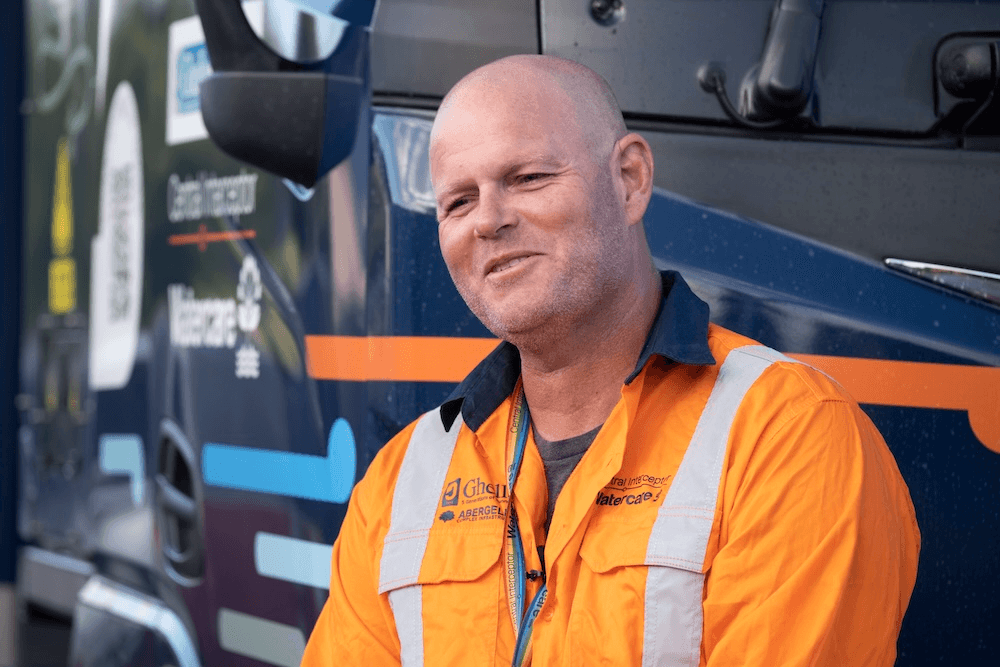 an older white man in an orange high vis shirt with a wistful smile 