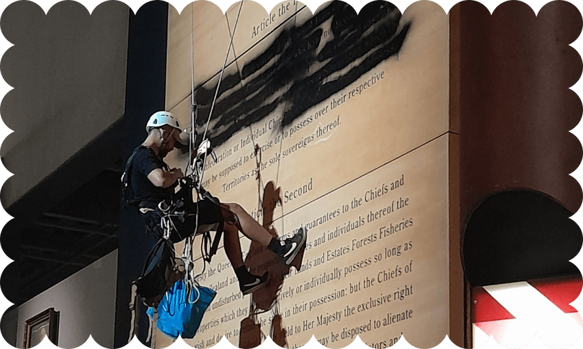 A protestor abseils down a multi story version of the Treaty of Waitangi at Te Papa, defacing it.