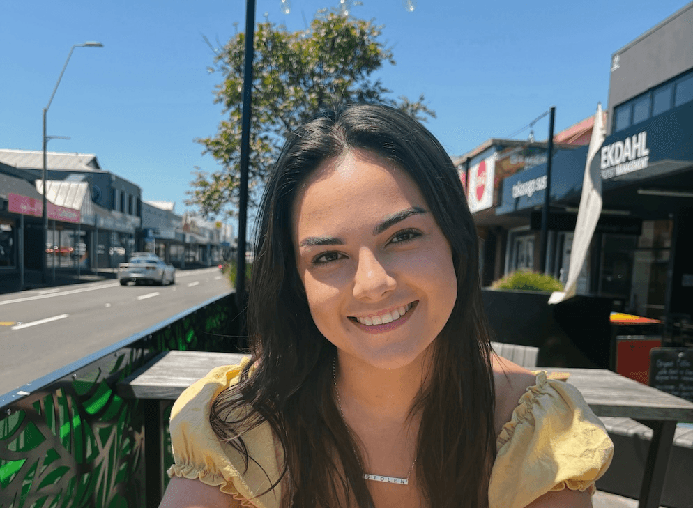 a brown skinned woman with dark hair smiling into the camera on a sunny day