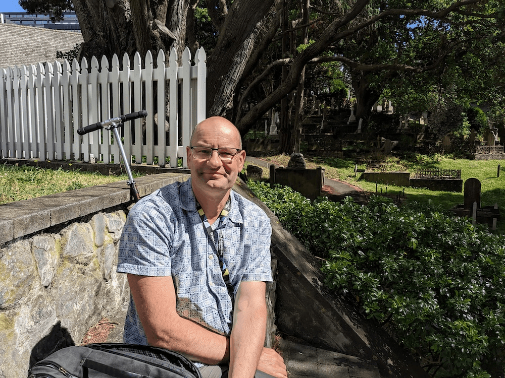 a bald man in a short sleeved shirt in a shady cemetery