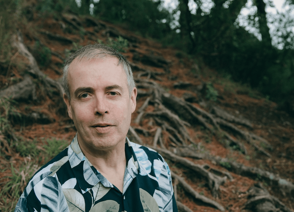 a grey haired man with trees in the background