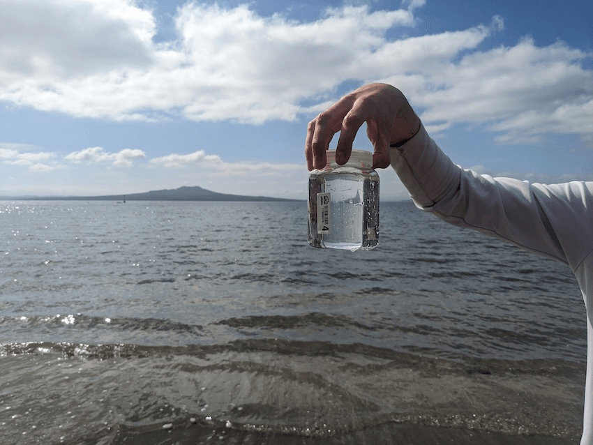 a hand holding a clear jar iwth rangitot in the background