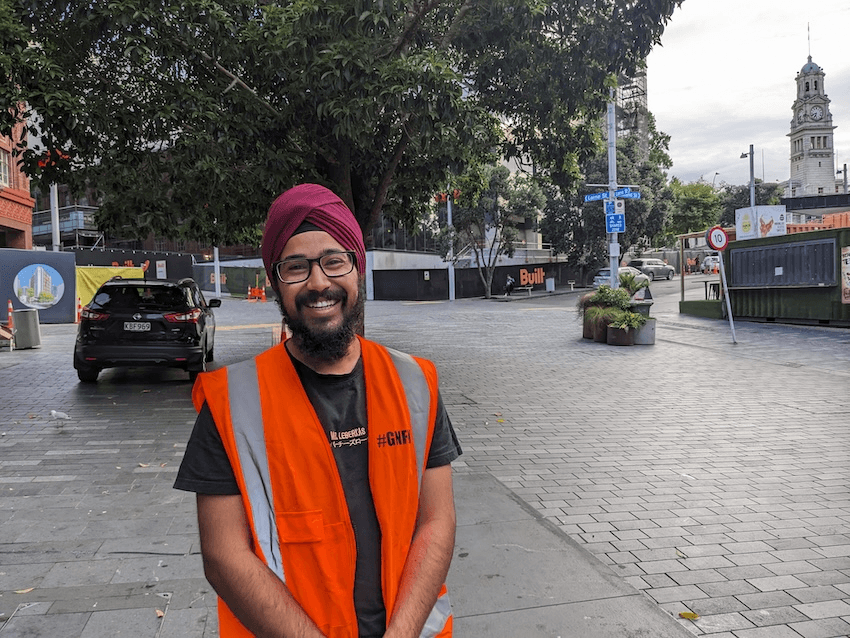 a smiling man in a red turban and orange hi vis vest - he looks kind and approachable 
