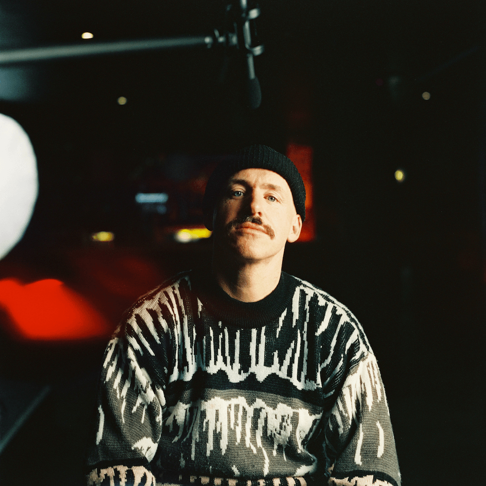 Tom Scott sits down for an interview for the Run It Back documentary wearing a jumper with crazy patterns on it.