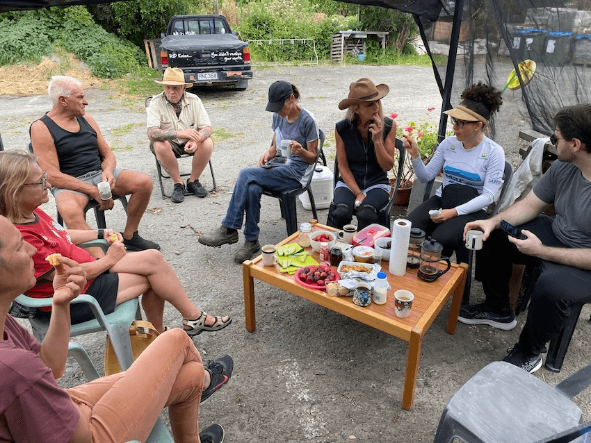 a group of people sitting around a table with greenery in the background and kai on the table