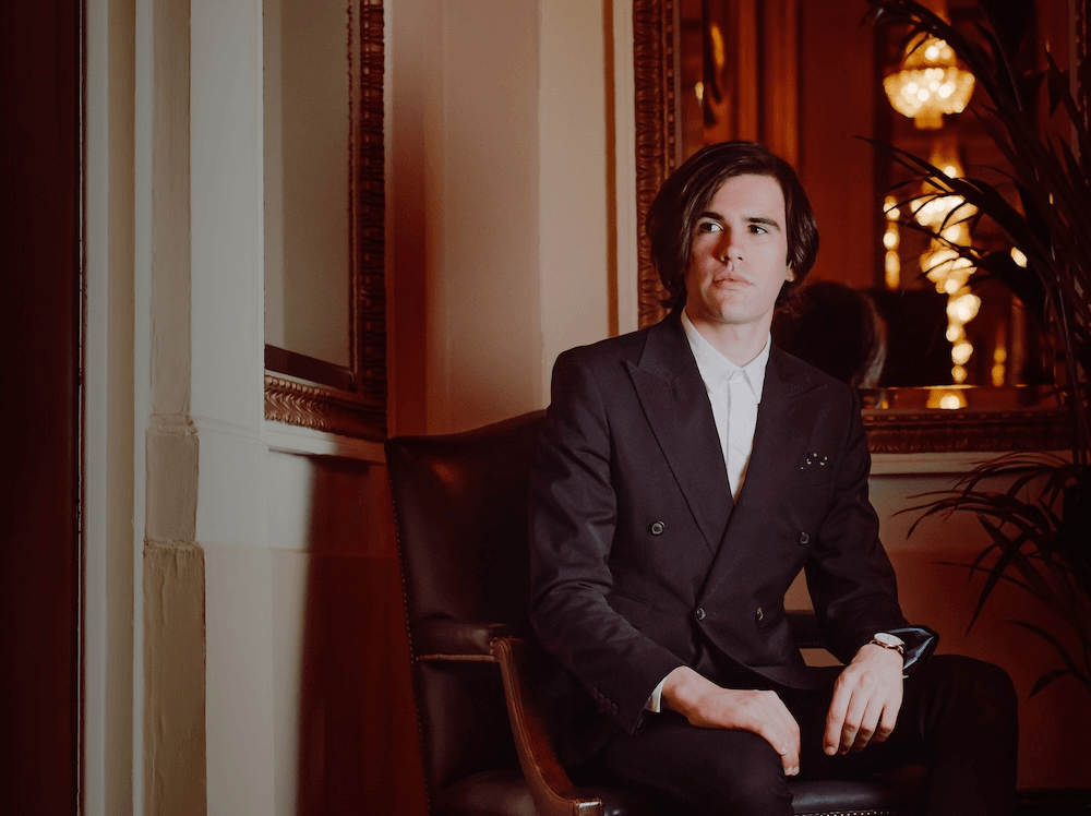 scott silven wearing a tailored blazer sitting on an armchair in a fancy looking house