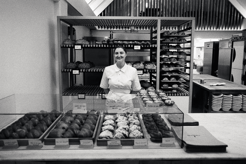 A baker stands behind her pastries in her bakery
