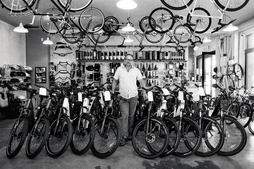 Mężczyzna stoi w swoim sklepie rowerowym otoczony rowerami
