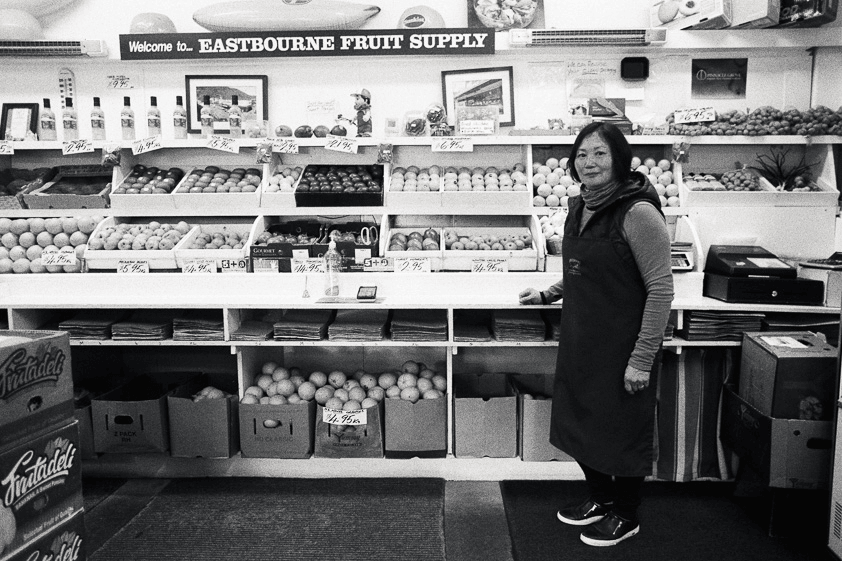 Kobieta stoi w sklepie z owocami i warzywami, a za nią towar