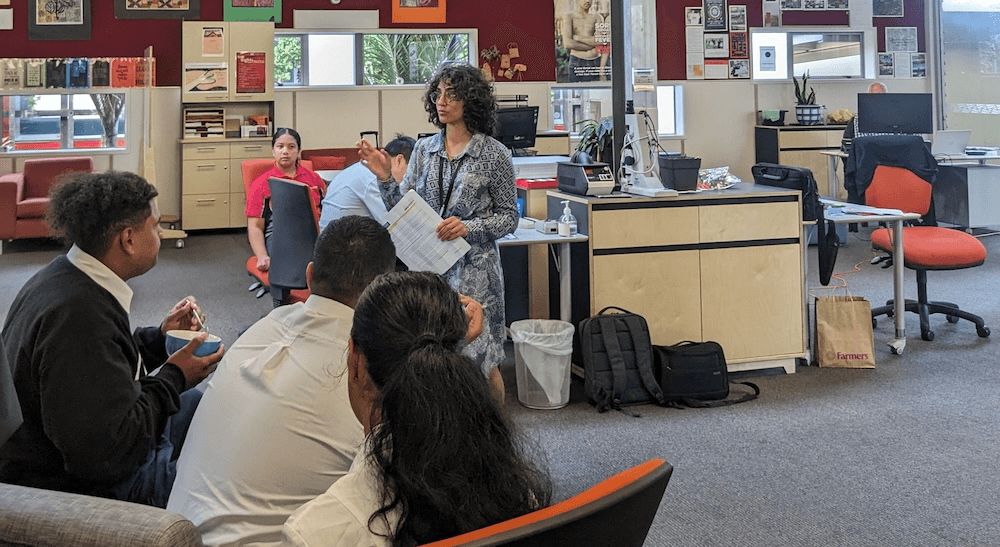 Sachi Rathod, a short woman with big bounchy curls, talks to students in uniforms in a school environment with their backs to the camera