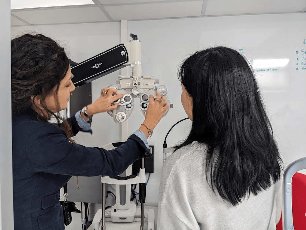 Germaine joblin uses an eye machine that puts different lenses in front of kids eyes while a younger optometry student looks on