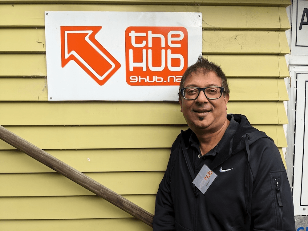 a brown skinned man in a black hoodie smiling in front of an orange sign