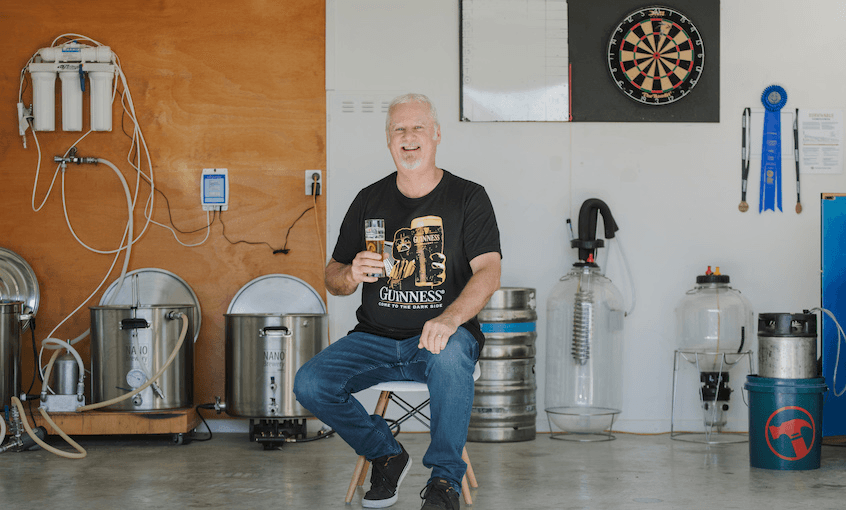 Craig Herron sits on a stool in his garage surrounded by home brew equipment. 