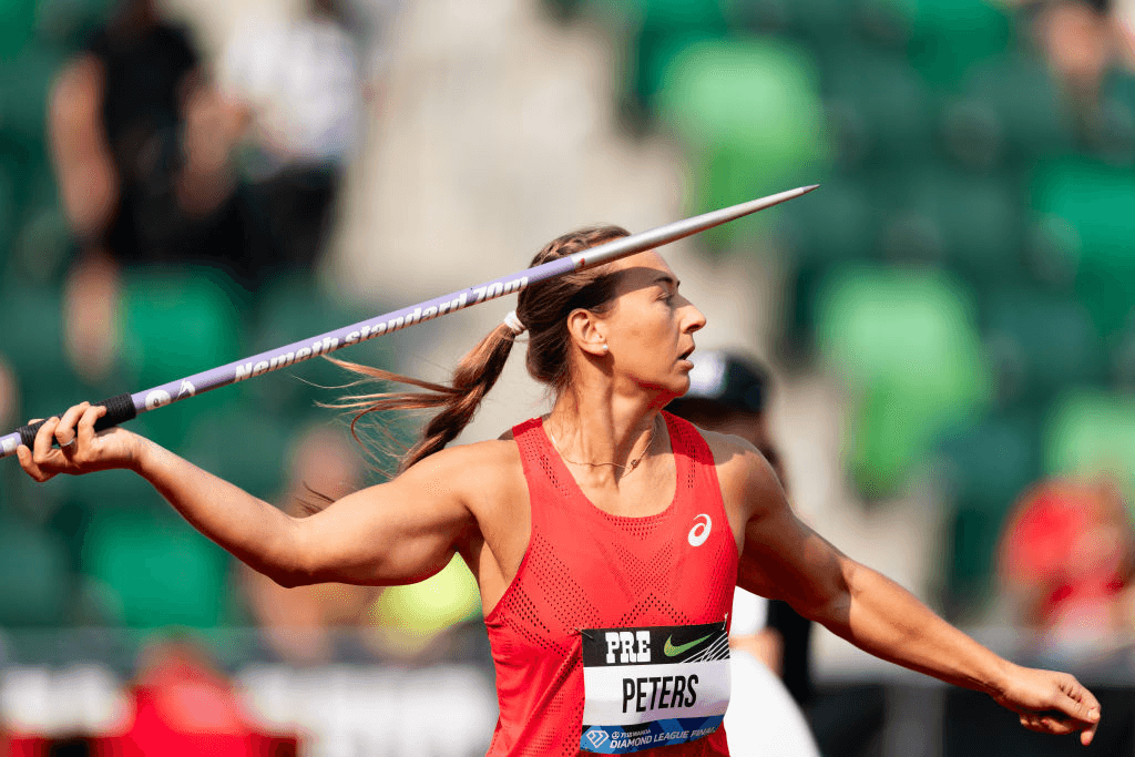 Tori Peeters stands holding a purple javelin and wearing a red singlet during competition