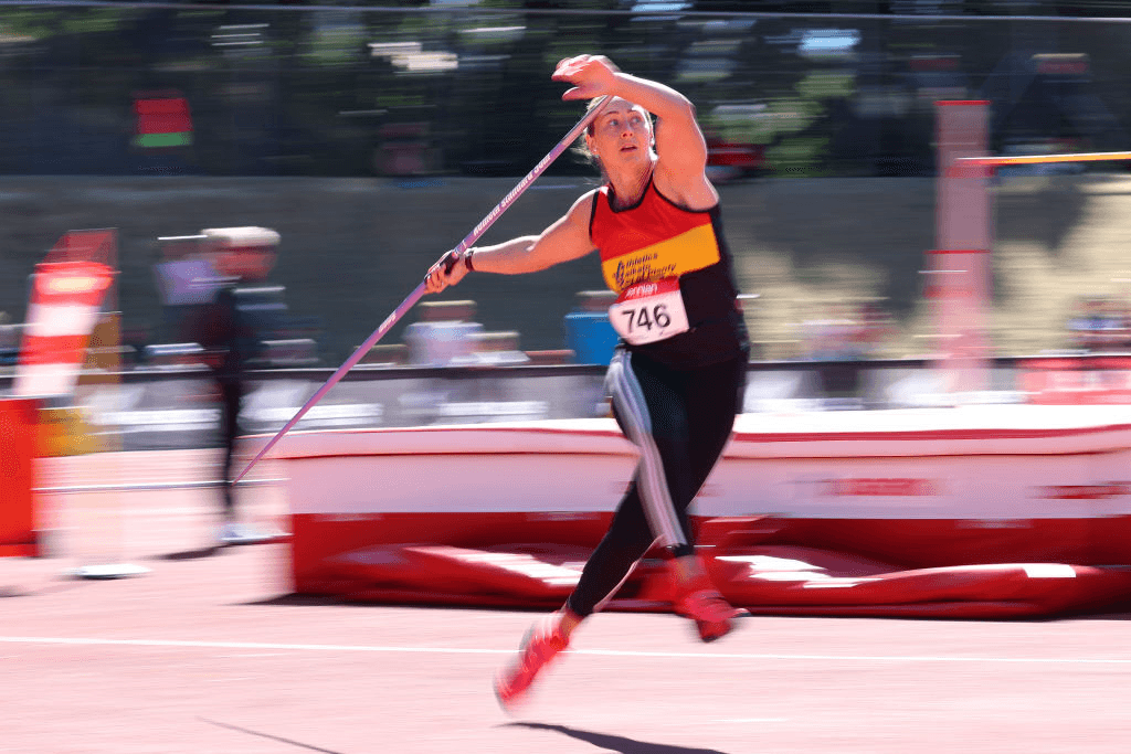 Tori Peeters wears a red, yellow and black singlet and strides through a javelin throw, holding the javelin aloft behind her