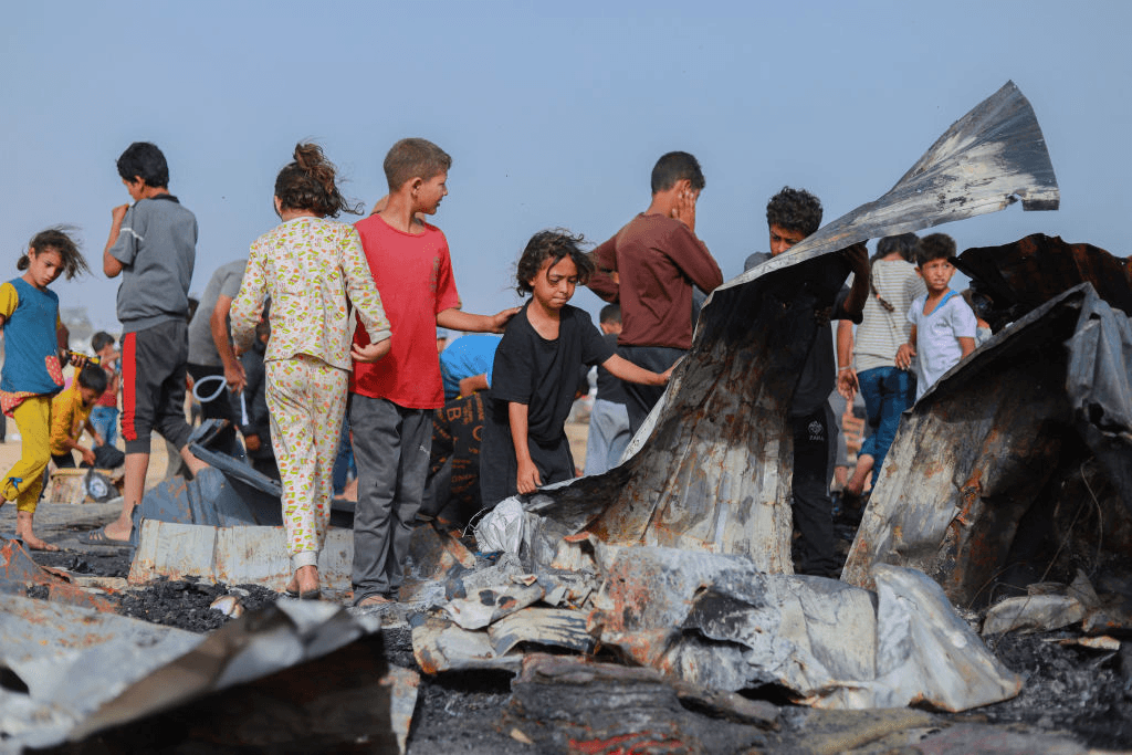 Children gathered around twisted and burnt corrogated iron